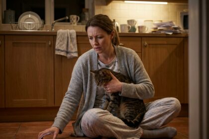 Femme inquiète tenant son chat malade dans la cuisine la nuit, cherchant une clinique vétérinaire d'urgence à Nice